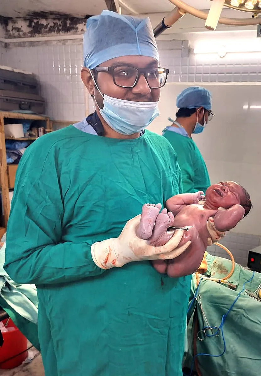 Clinician holding a newborn in an operating-theatre setting